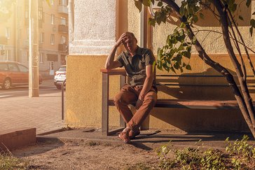 Ein alter Mann sitzt erschöpft auf einer Bank in der Sommerhitze.