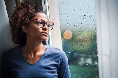 Eine Frau schaut aus dem Fenster und leidet besonders stark unter Symptomen wie Stimmungsschwankungen, Reizbarkeit oder depressiven Verstimmungen – jeden Monat eine zermürbende Krise. Dies ist die so genannte Prämenstruelle Dysphorische Störung (PMDS).