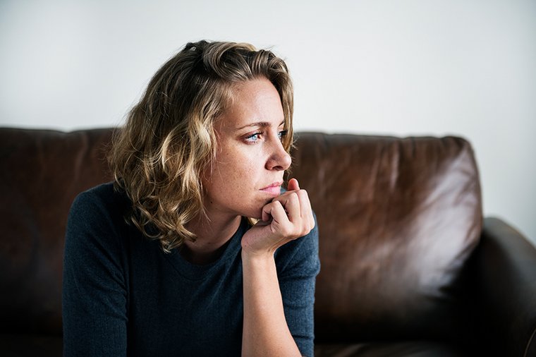 Eine junge Frau sitzt nachdenklich auf einem Sofa.