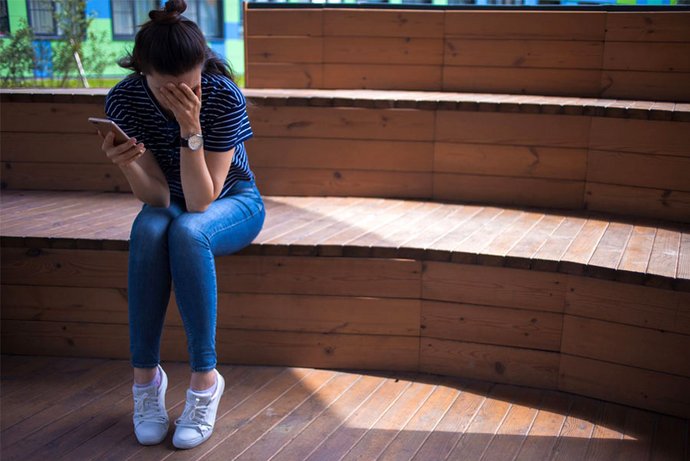 Eine junge Frau ist nach dem Blick auf ihr Smartphone verzweifelt. Die gesundheitlichen Beeinträchtigungen von Stalking-Betroffenen sind erheblich.