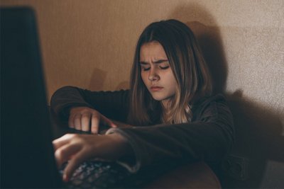 Eine Jugendliche sitzt vor einem Computer und gibt etwas auf der Tastatur ein.