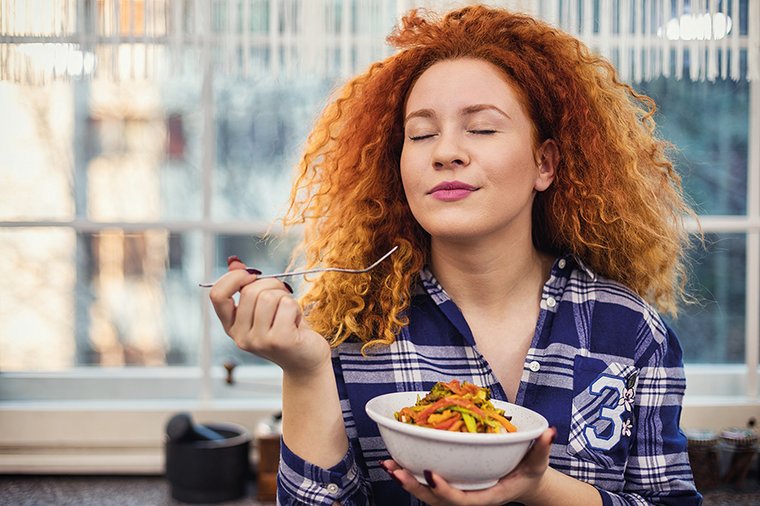 Eine junge Frau isst genüsslich einen Salat. 