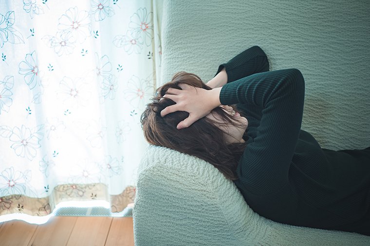 Ein Frau liegt schmerzgeplagt auf dem Sofa.