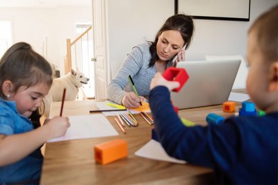 Eine Frau arbeitet im Home-Office und passt gleichzeitig auf ihre beiden Kinder auf.