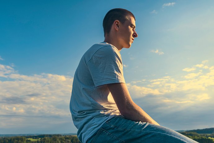 Ein junger Mann sitzt in der Natur und die Sonne scheint ihm ins Gesicht.