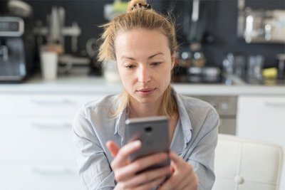 Frau sitzt in der Küche und schaut auf ihr Smartphone