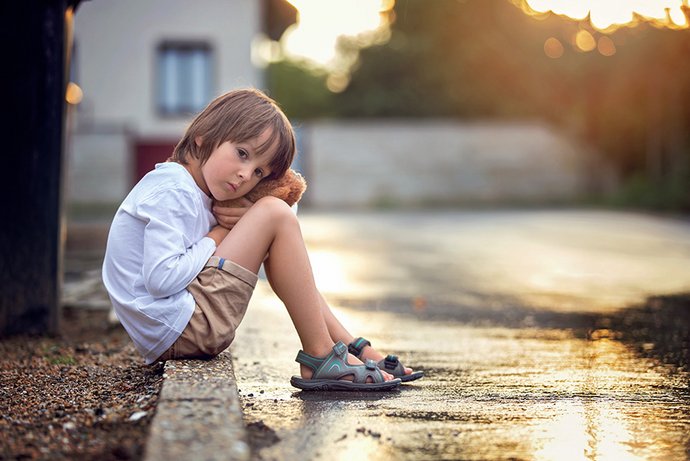 A small child sits sadly by the side of the road.