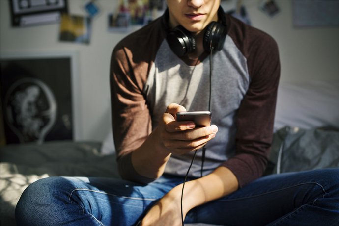 Ein Jugendlicher sitzt in seinem Zimmer auf dem Bett und nutzt sein Smartphone.