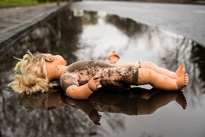 Eine Puppe ist mit Schlamm bespritzt und liegt in einer großen Pfütze. 