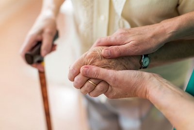 Eine Frau hält einer älteren Frau am Stock die Hand und beruhigt sie durch Berührung.