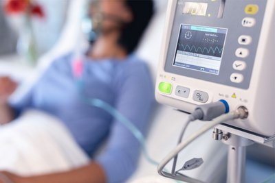 Eine Frau liegt mit schwerer SARS-CoV2-Infektion auf dem Krankenbett und ist an eine Beatmungsmaschine angeschlossen. 