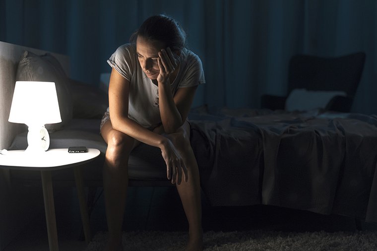 Eine Frau sitzt in der Dunkelheit auf ihrem Bett.