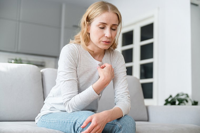 Eine Frau im mittleren Alter sitzt schmerzgeplagt auf dem Sofa.