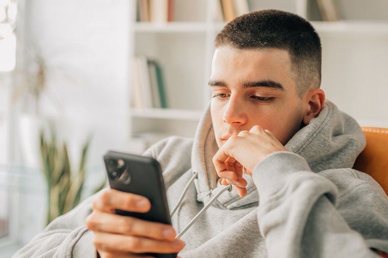 Ein junger Mann starrt nachdenklich auf sein Smartphone. 