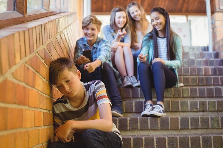 Junge sitzt traurig auf einer Treppe und wird von einer Gruppe ausgelacht.