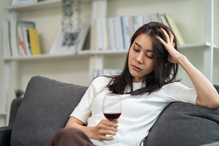 Eine junge dunkelhaarige Frau sitzt auf einem Sofa und hat ein Glas Rotwein in der Hand. 
