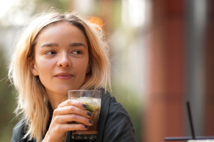 Junge Frau mit orangenen Jahren trinkt einen Cocktail.